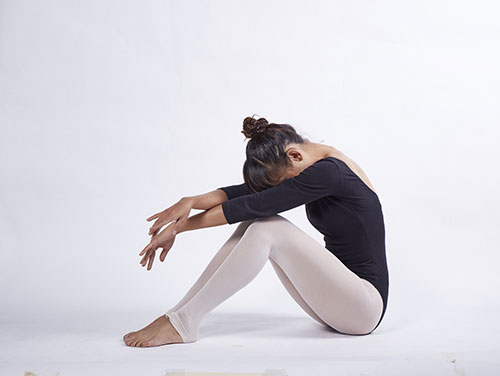 en kvinna i body och leggings sitter pa golvet med haret uppsatt mot en vit bakgrund