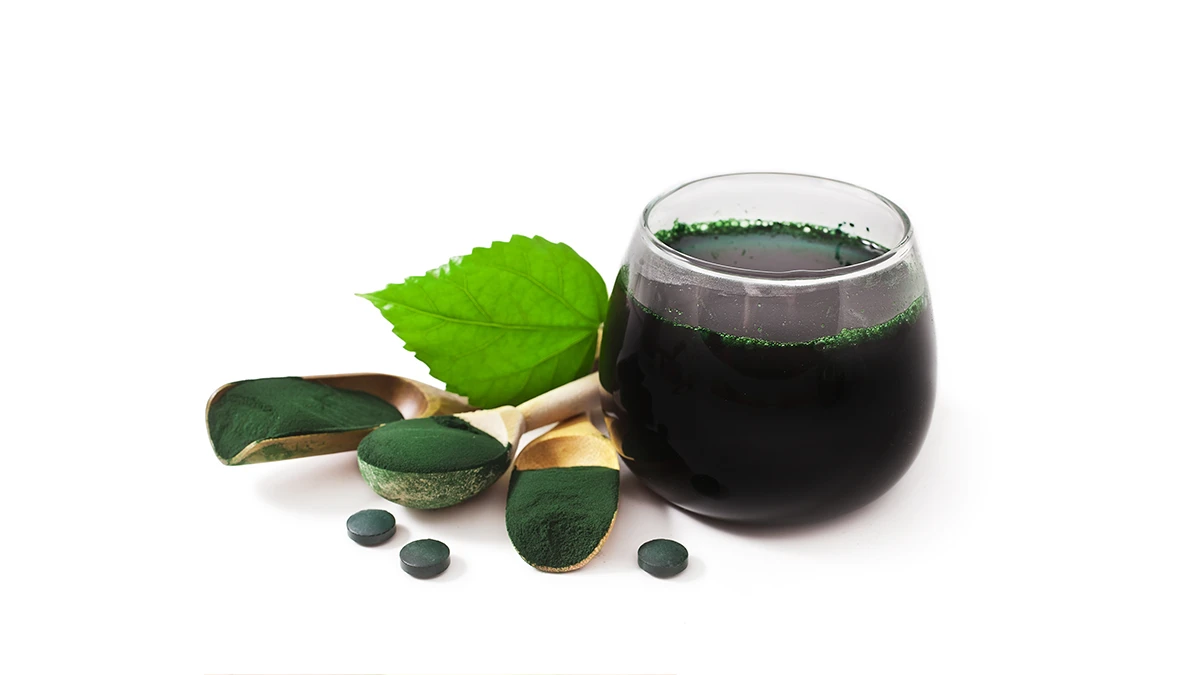 Ett glas med spirulina, tre skedar spirulinapulver på bordet och två spirulinatabletter – effekten av spirulina för att gå ner i vikt.