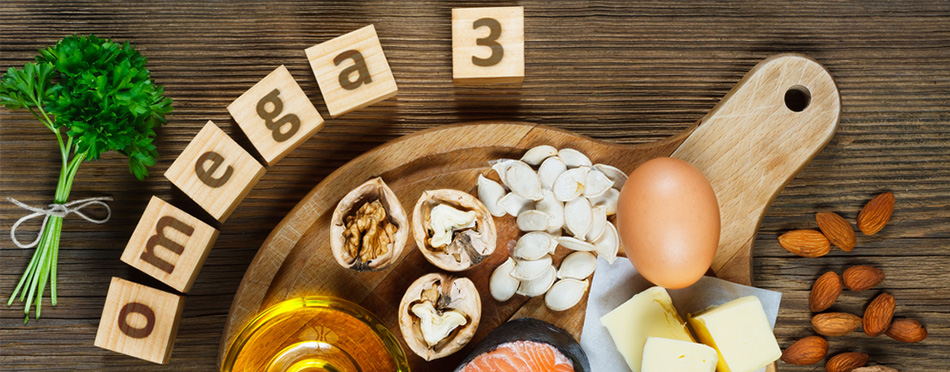 En bild på en skärbräda med ägg, nötter, olja, fisk och på bordet är det kuber som stavar till omega 3, och broccoli samt mandlar